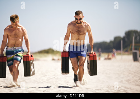 Starke Crossfit Jungs heben schwere Kanister außerhalb am Strand. Muskulöse aktive Menschen in 20er Jahren Ausbildung weiterhin gesunde Leben Stockfoto