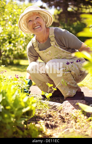 Ältere Frau glücklich, arbeiten mit Pflanzen in ihrem Garten - alte Frau im Garten im Hinterhof Stockfoto