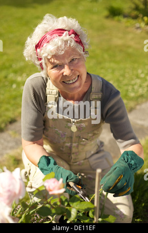 Schöne ältere Frau kümmert sich um für die Pflanzen in ihrem Hinterhofgarten - Natur Stockfoto