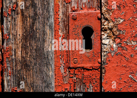 Altes Türschloss, Schlüsselloch auf einem verwitterten Holztür mit Fragmenten von roter Farbe Stockfoto