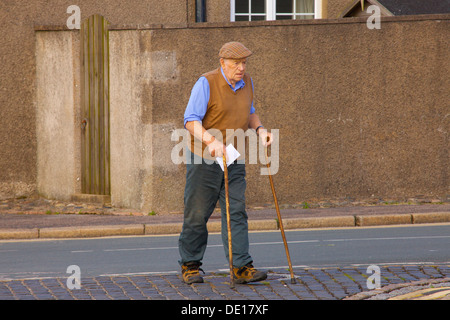 Alter Mann mit Stöcken, beim Überqueren der Straße um einen Brief zu schreiben. Nordengland. Stockfoto