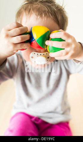 Kleines Mädchen, 3 Jahre alt, Spaß haben und versteckt sich hinter bunten Bällen Stockfoto