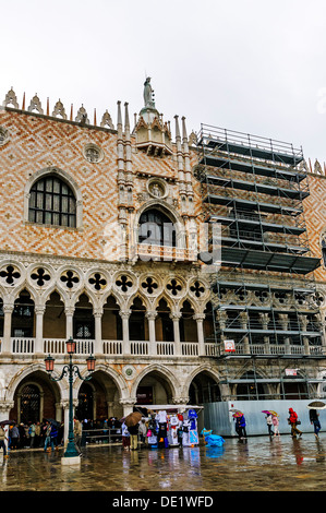 Touristen in die Warteschlange in der Spielhalle auf Tour durch das Innere des Dogenpalastes und den Regen fällt auf die Piazzetta di San Marco zu vermeiden Stockfoto