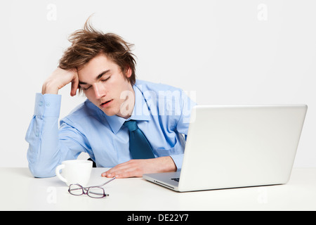 Jungen Mann im Büro mit dem Laptop auf seine front und schlafen erschöpft Stockfoto