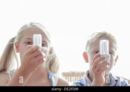 Mädchen und jungen halten Energiesparlampen vor den Gesichtern Stockfoto