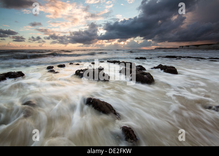 Wellen brechen an einem felsigen Strand bei Sonnenuntergang Stockfoto