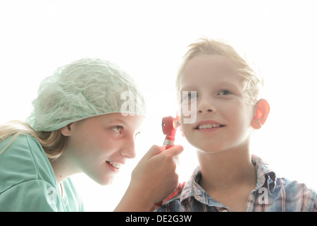 Mädchen und Jungen spielen Arzt mit dem Mädchen, die Prüfung der junge Ohr Stockfoto