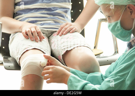 Mädchen und Jungen spielen Arzt mit dem jungen gekleidet als Arzt einen Verband um das Mädchen Knie wickeln Stockfoto