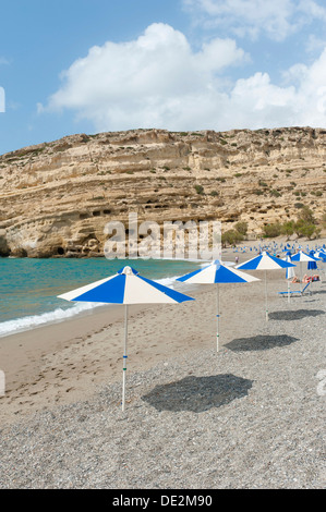 Neolithischen Wohnhöhlen in gelbem Sandstein, Sonnenschirme am Strand von Matala, ehemaligen Gelände des libyschen Meeres Hippies, Kreta, Stockfoto