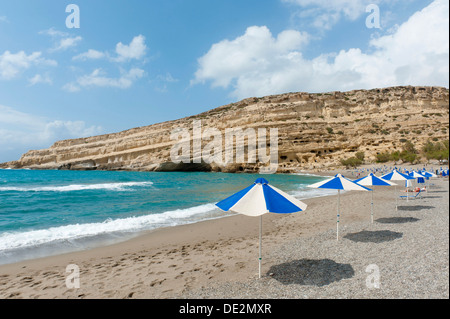 Neolithischen Wohnhöhlen in gelbem Sandstein, Sonnenschirme am Strand von Matala, ehemaligen Gelände des libyschen Meeres Hippies, Kreta, Stockfoto