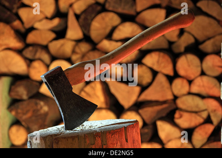 Axt auf einem Baumstamm, gestapeltes Brennholz auf der Rückseite Stockfoto