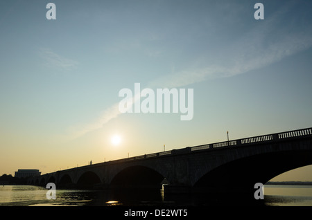 Die Sonne steigt über Memorial Bridge, gesehen aus Arlington, VA, Seite, wie es erstreckt sich über den Potomac. Das Lincoln Memorial ist auf der anderen Seite auf der linken Seite des Rahmens Silhouette. Stockfoto