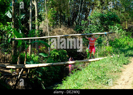 kleiner Junge spielt auf einer klapprigen Bambusbrücke über kleine Fluss im ländlichen Dorf Java Indonesien Stockfoto