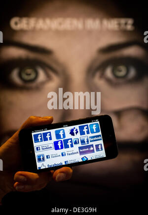 ILLUSTRATION - ein Mann hält eine Smartphone mit Facebook-Logo vor einem Plakat lesen "Gefangen im Netz" auf dem internationalen Cyberbullying-Kongress in Berlin, Deutschland, 11. September 2013. Die Cyber-Mobbing-Konferenz diskutiert wie man Mobbing im Internet und wie sie schikaniert Internetnutzer. Foto: HANNIBAL Stockfoto