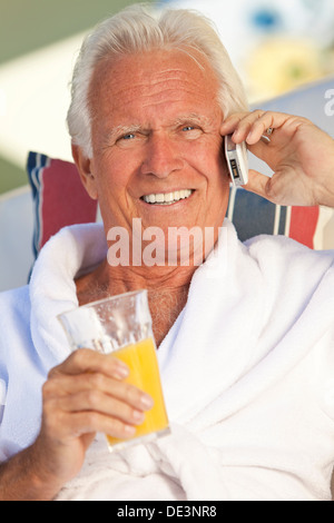 Attraktive gut aussehend senior glücklich im weißen Bademantel, draußen, Lächeln, reden auf seinem Handy Orangensaft trinken Stockfoto