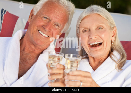 Ältere Mann und Frau Brautpaar auf Kur im weißen Bademantel lächelnd und Champagner trinken Stockfoto