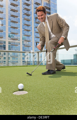 Erfolgreicher Geschäftsmann oder Mann in einem Anzug, Golfen auf corporate Putting Green auf dem Dach eines Wolkenkratzers Bürogebäudes Stockfoto
