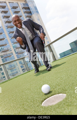 Afrikanische amerikanische Geschäftsmann oder Mann in einem Anzug, Golfen auf corporate Putting Green auf dem Dach eines Wolkenkratzers Bürogebäudes Stockfoto