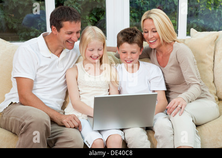 Eine attraktive, Familienglück von Mutter, Vater, Sohn und Tochter sitzen auf einem Sofa zu Hause Spaß per Laptop oder computer Stockfoto