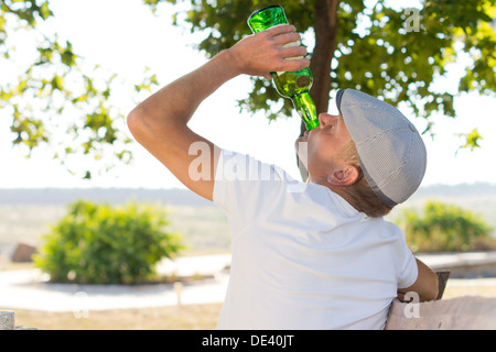 Rückansicht eines alkoholischen Mann trinken aus einer Flasche Weißwein in den Park im Sommer Stockfoto