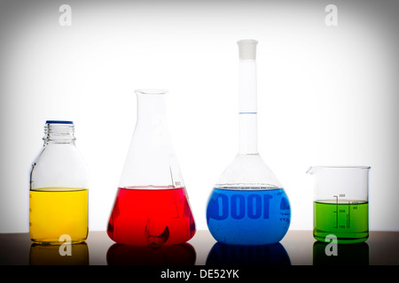 Vier Messen Gläser auf einem Tisch ein chemisches Laboratorium mit roten, gelben, blauen und grünen Flüssigkeit auf weißem Hintergrund Stockfoto