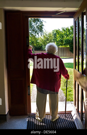 ÄLTERE ALLEIN EINGANGSTÜR WARTET UNSICHER nachdenklich ältere ältere ältere Dame, die allein mit Gehstock steht, hält an der offenen Tür ihrer Wohnung inne Stockfoto