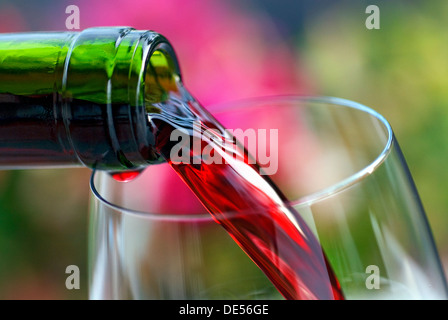 Gießen Rotwein in ein Weinglas mit Gartenblumen im Hintergrund Stockfoto