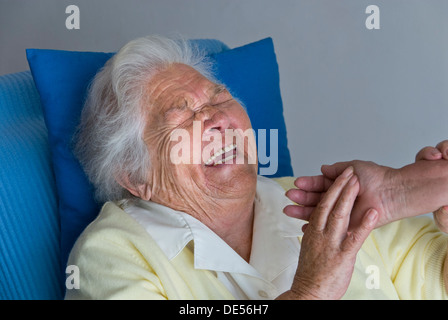 Alte ältere glücklich lachende ältere Dame Frau hält beruhigende Hand der Pflegebegleiterin in ihrem komfortablen Zimmer Stockfoto