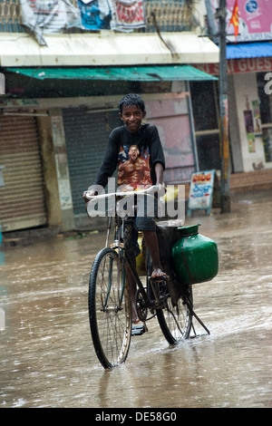 Niedrigen Kaste Indianerdorf junge Radfahren durch eine überschwemmte Straße während des Monsuns. Puttaparthi, Andhra Pradesh, Indien Stockfoto