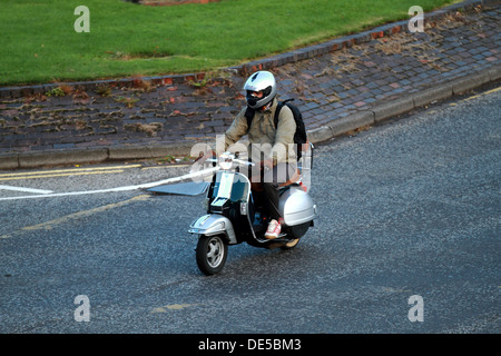 Ein Mann auf einem Moped Roller Fahrrad fährt zur Arbeit trägt einen Helm und schlichte Kleidung Stockfoto