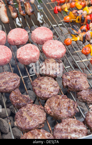 Saftige durchgebratenes Hacksteaks, Würstchen und Döner Kochen auf einem großen offenen Holzkohlegrill catering für eine Party. Stockfoto