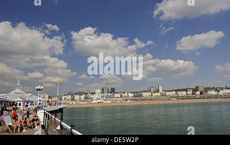 Touristen, die zum Sonnenbaden auf der Brighton Pier mit Strand im Hintergrund East Sussex England Stockfoto