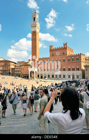 Touristen auf der Piazza del Campo, dem zentralen Platz der Stadt Siena, Toskana, Italien. Torre del Mangia Turm erhebt sich hinter Stockfoto