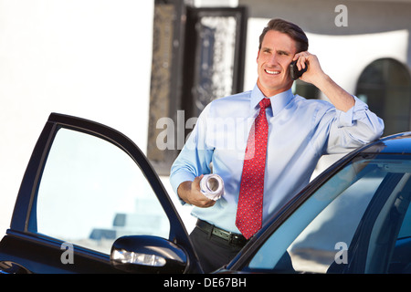 Ein erfolgreicher Geschäftsmann oder Architekt hält Pläne & reden auf seinem Handy von einem Auto Stockfoto