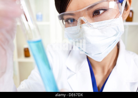 Eine chinesische asiatische medizinische oder wissenschaftliche Forscherin oder Arzt mit Blick auf ein Reagenzglas blaue Flüssigkeit in einem Labor Stockfoto