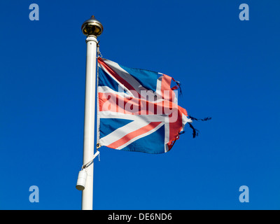 Hin-und hergerissen britischen Union Jack Flagge auf eine Fahnenstange mit blauem Himmel hinter Stockfoto