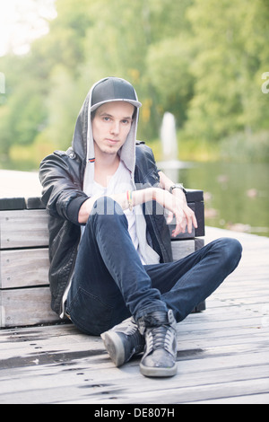 Lebensstil-Porträt des Jünglings in Lederjacke sitzt in einem Park, Blick in die Kamera Stockfoto