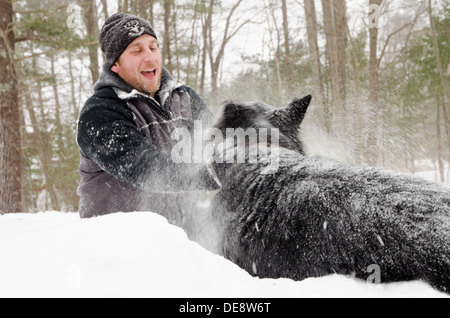 Ein Mann und ein Hund spielen im Schnee in einem Schneesturm. Stockfoto