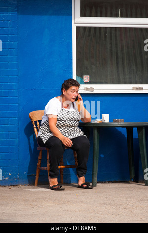 East End von London Fisch Insel Hackney Wick im mittleren Alter Dame sitzt außerhalb Blue Cafe Tisch Stuhl Mobiltelefon Tabelle Tasse Kaffee Tee Stockfoto