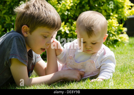 acht Jahre alter Junge mit acht Monate alte Schwester auf Rasen im Garten Stockfoto