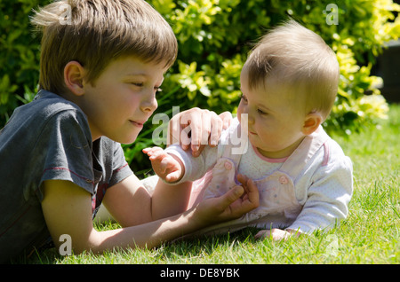 acht Jahre alter Junge mit acht Monate alte Schwester auf Rasen im Garten Stockfoto