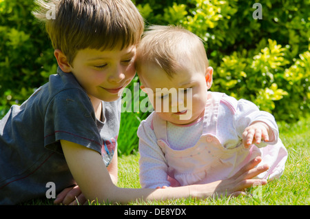 acht Jahre alter Junge mit acht Monate alte Schwester auf Rasen im Garten Stockfoto