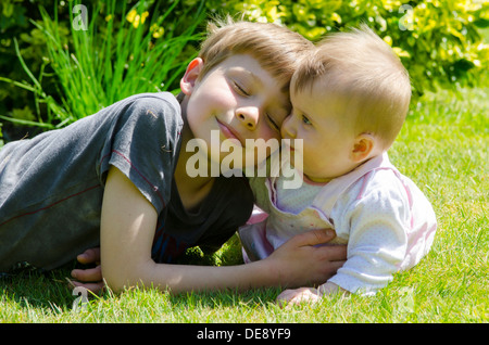 acht Jahre alter Junge mit acht Monate alte Schwester auf Rasen im Garten Stockfoto