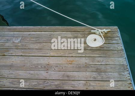 Ein weißes Seil ist bis auf eine hölzerne Dock mit einem Ende vorbei über das tiefgrüne Wasser führt zu das Boot nicht im Bild aufgewickelt. Stockfoto