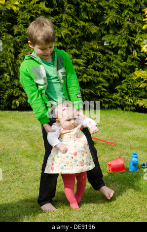 acht Jahre alter Junge Geschwister mit acht Monate alte Schwester spielen im Garten Stockfoto