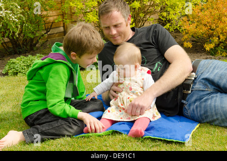 Vater mit acht Jahre alten Sohn und acht Monate alte Tochter draußen im Garten in der Sonne Stockfoto