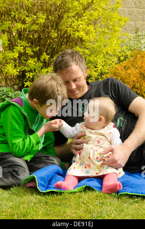 Vater mit acht Jahre alten Sohn und acht Monate alte Tochter draußen im Garten in der Sonne Stockfoto