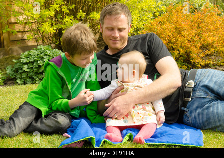 Vater mit acht Jahre alten Sohn und acht Monate alte Tochter draußen im Garten in der Sonne Stockfoto