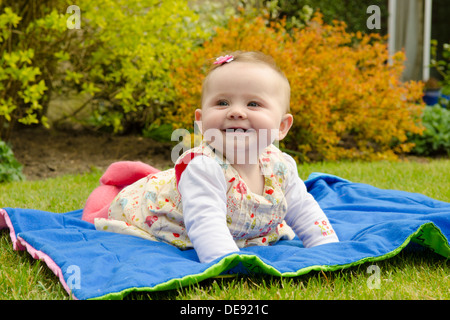 acht Monate altes Babymädchen auf Decke draußen im Garten Stockfoto