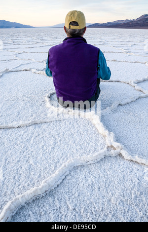 Ein Mann sitzt in geometrischen Mustern Salzpfanne in der Nähe von Badwater im Death Valley Nationalpark, Kalifornien. Stockfoto